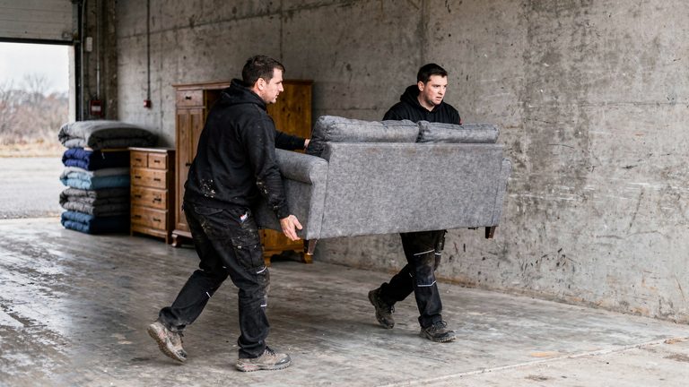 Zwei Mitarbeiter tragen gemeinsam ein Sofa zum Transporter